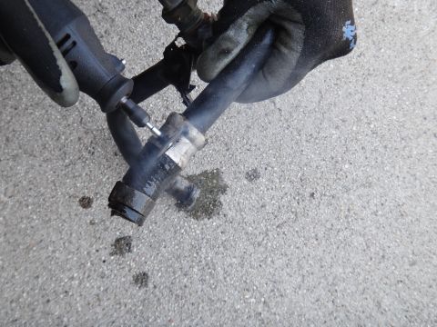 1993 Ford Taurus - A gloved hand uses a rotary tool to cut an automotive hose with a metal clamp.