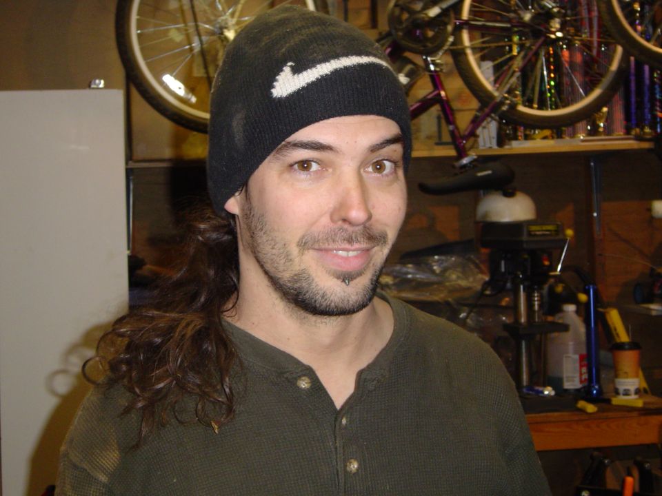 Young man in dark Nike beanie and green henley in a bike workshop