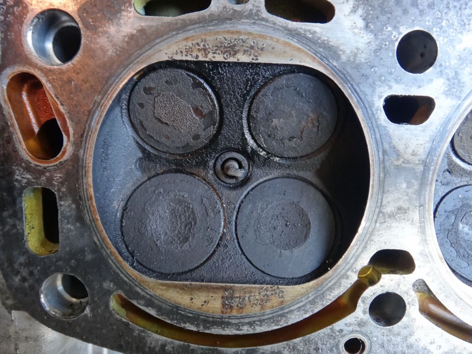 Close-up of an engine cylinder head showing four valves and carbon buildup