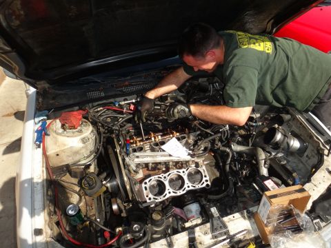 1993 Ford Taurus - Mechanic performs engine work on a white vehicle with the hood open, surrounded by tools and engine components.