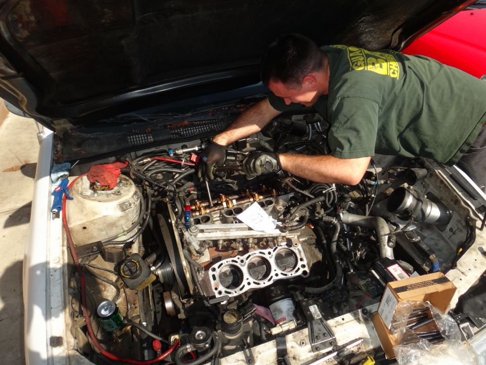 Mechanic working on a disassembled engine, white car, open hood, tools and parts scattered