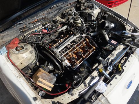 1993 Ford Taurus - The engine bay of a white 1993 Ford Taurus shows disassembled engine components and various tools.