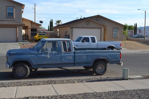 1981 Ford F-250 - blue 1980s Ford crew/extended cab pickup and a tan Ford pickup parked on a suburban desert street.
