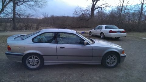 2000 Mercury Grand Marquis - Two cars parked outdoors, a silver coupe in the foreground and a white sedan in the background. The white sedan appears to be a 2000 Mercur…