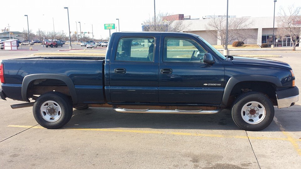 Dark blue pickup truck, side view, showing four doors and a long bed. The truck has chrome running boards and fender flares