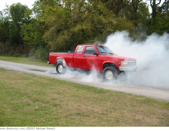 Red dually extended-cab pickup doing a smoky burnout on a rural road
