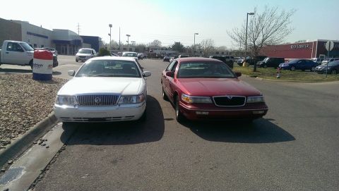 2000 Mercury Grand Marquis - Two Mercury Grand Marquis sedans are parked in a lot, with a white one on the left and a red one on the right.