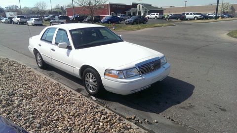 2000 Mercury Grand Marquis - A white sedan is parked on the side of the road with a gravel shoulder and a paved intersection.