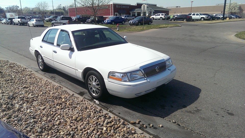 White sedan parked on a street, angled from the front-left. The car has chrome grille and alloy wheels