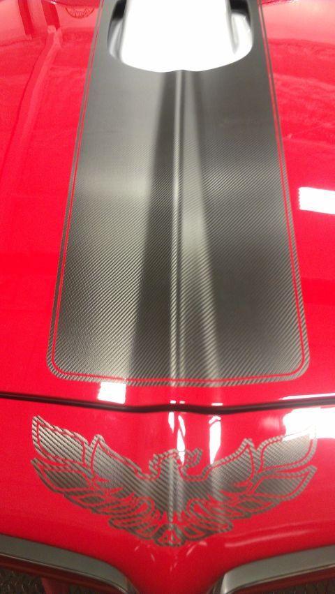 1972 Pontiac Trans Am - Close-up of a red car's hood, showing a black stripe and a distinctive bird decal, likely from the 1970s.