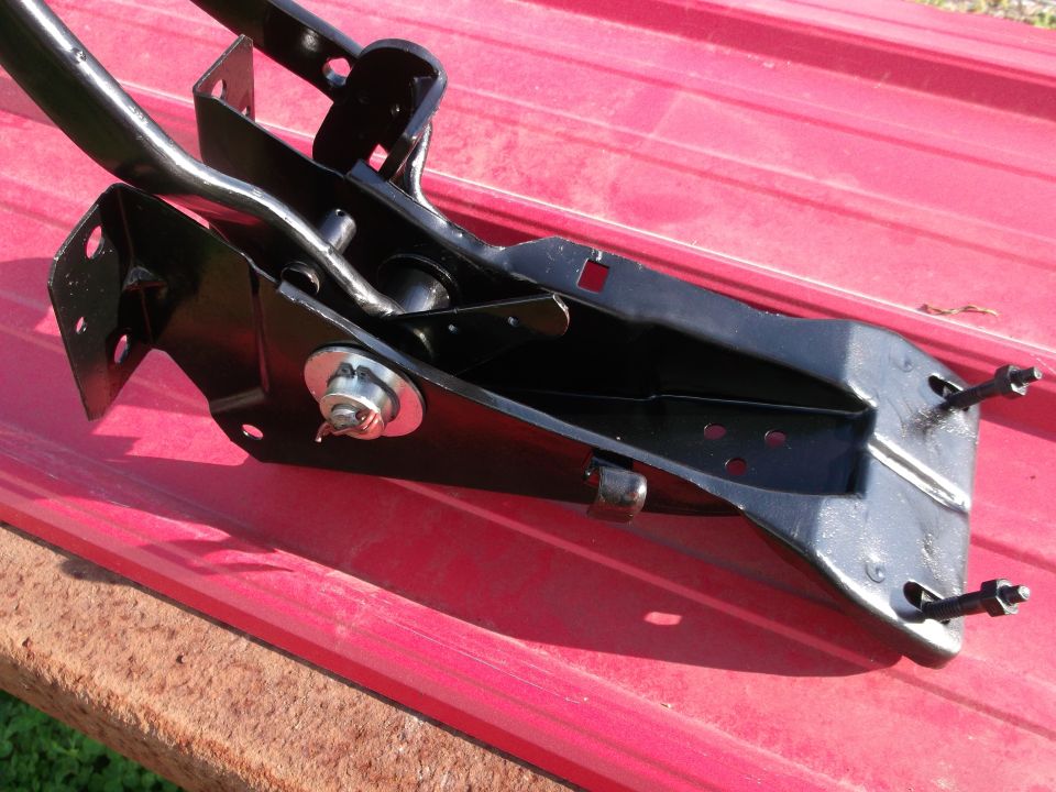 Black metal clutch pedal assembly with linkage and bolts, resting on a red surface