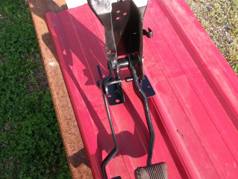 1967 Ford Mustang - Assembly of brake and clutch pedals, likely for a classic car, photographed on a red corrugated surface.