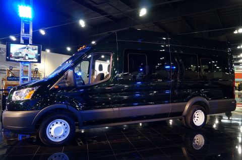1993 Ford Taurus - A dark green passenger van is displayed indoors under bright lights, reflecting on the glossy floor.