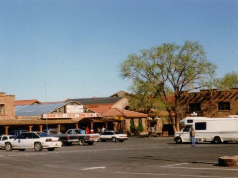 1991 Ford LTD Crown Victoria - Several vehicles, including a white 1991 Ford Crown Victoria, are parked outside a trading post.