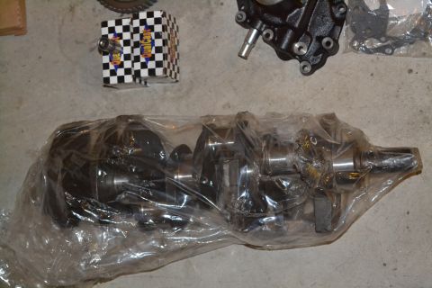1981 Ford F-250 - Engine parts laid out on a concrete floor, including a crankshaft and a component with mounting holes.