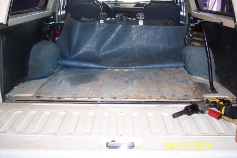 1990 Ford Bronco - The cargo area of a 1990 Ford Bronco shows a blue mat covering a metal floor, with tools visible at the tailgate.