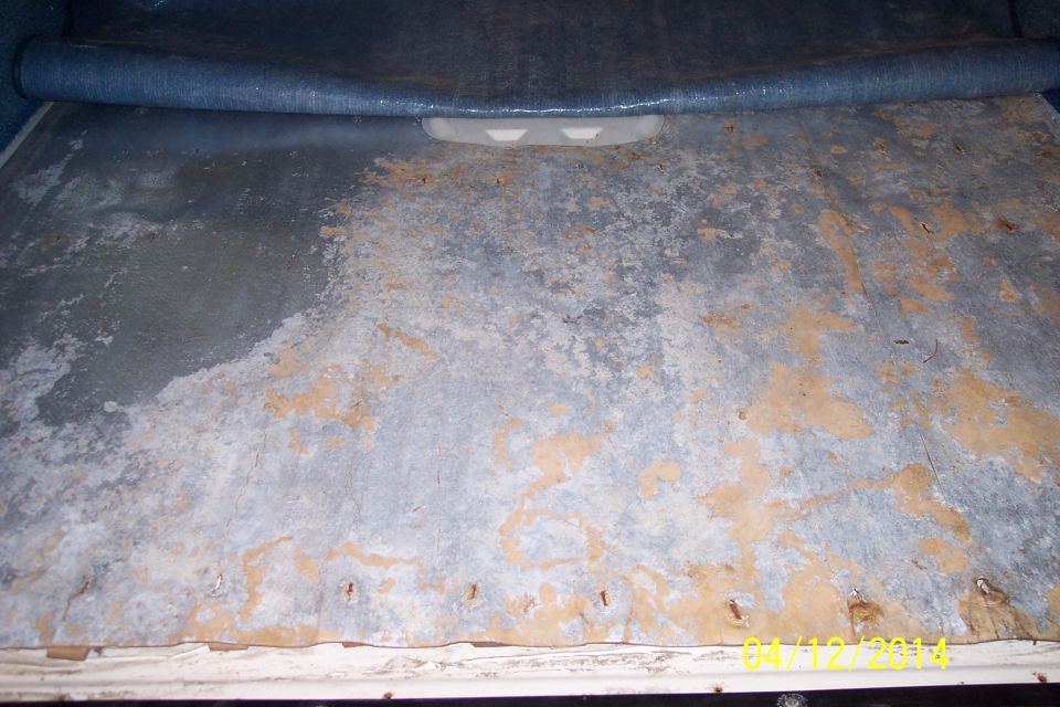 Corroded metal floor panel with some blue carpet material rolled up at the top
