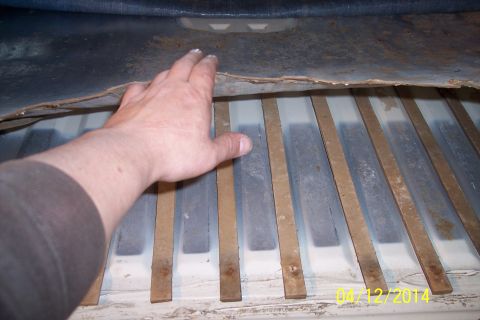 1990 Ford Bronco - A hand is shown reaching into the underside of a vehicle, revealing structural ribs and insulation material.