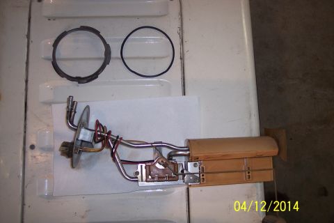 1990 Ford Bronco - Fuel pump sending unit assembly and related parts laid out on a white surface.