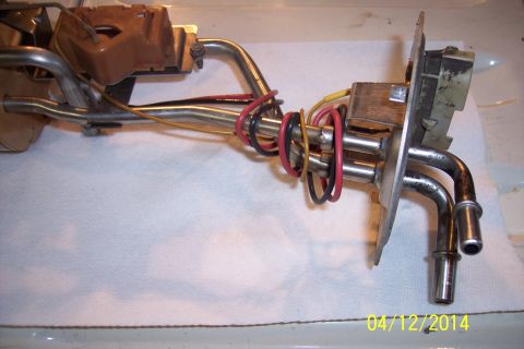 1990 Ford Bronco - A fuel pump assembly with metal lines and electrical wires is shown on a white surface.