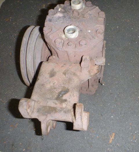 1964 Mercury Monterey - A rusty air conditioning compressor with a pulley is shown against a dark, textured background.