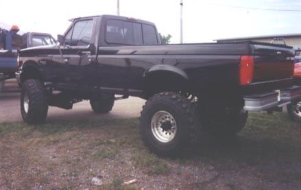 1979 Ford Bronco - This lifted black pickup truck is parked outdoors with another vehicle in the background.