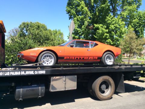 1968 Ford Mustang - An orange De Tomaso Pantera is transported on a flatbed tow truck.