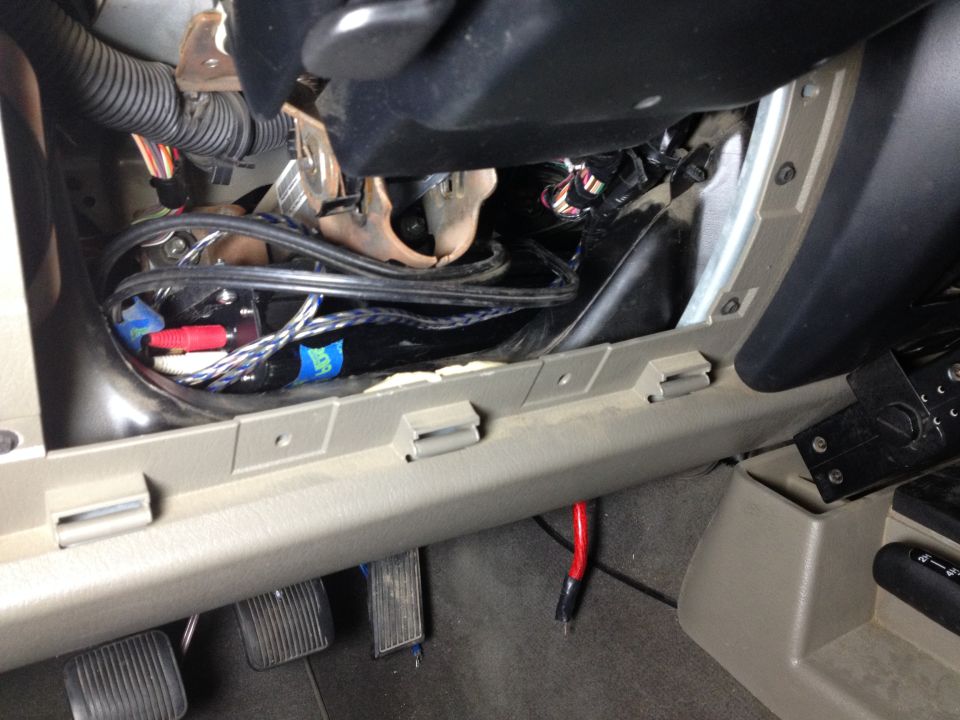 Car interior showing wiring and RCA cables under the dashboard near the pedals