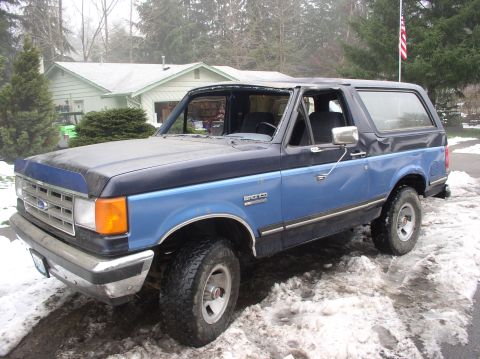 1988 Ford Bronco - This Ford Bronco is parked outside a house in a snowy environment. The vehicle has a two-tone paint scheme.