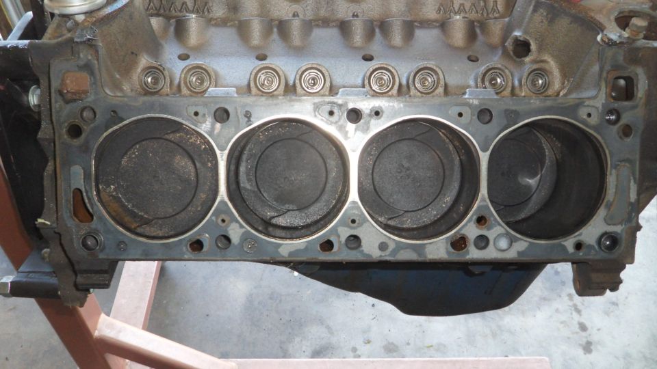 Engine block with four visible pistons, some showing carbon buildup and cracks