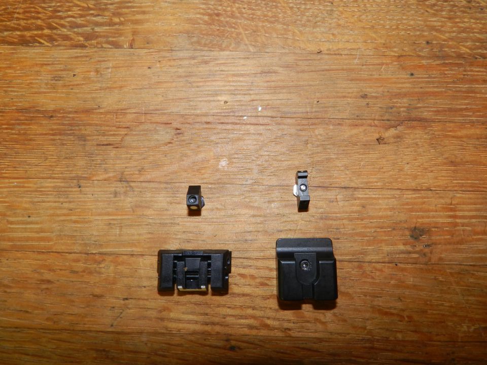 Four black plastic automotive clips on a wooden surface. Two small clips are above two larger clips