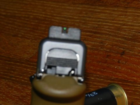 1996 Ford Bronco - The image shows the rear sight of a pistol, with a green dot sight, resting on a wooden surface next to a shotgun shell.