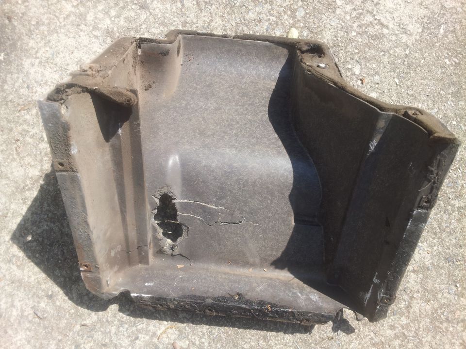 Damaged black plastic automotive part with a hole and cracks, viewed from above
