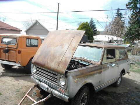 1972 International Scout II - Two International Scout SUVs are parked in a yard, one with its hood open, revealing the engine.