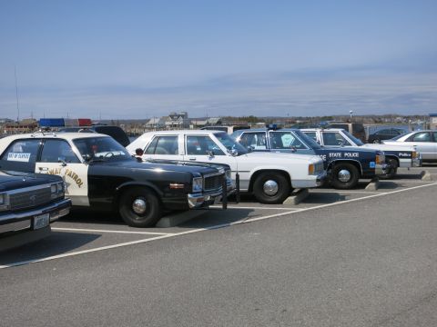 1991 Ford LTD Crown Victoria - lineup of vintage police cars in a lot, including a black-and-white Highway Patrol cruiser, white sedans and a blue STATE POLICE car.