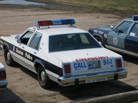 1991 Ford LTD Crown Victoria - Rear three-quarter view of a Boston Police sedan, unit 7087, marked 'Emergency Call 9-1-1' and 'Out of Service'.