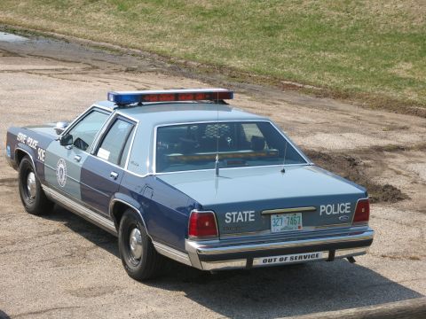 1991 Ford LTD Crown Victoria - Rear quarter view of a two-tone blue State Police Ford sedan marked 'Out of Service' on a gravel lot.
