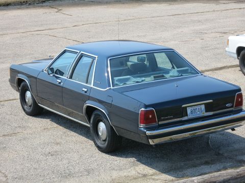 1991 Ford LTD Crown Victoria - Rear three-quarter view of a dark blue Ford LTD Crown Victoria sedan parked on cracked pavement.