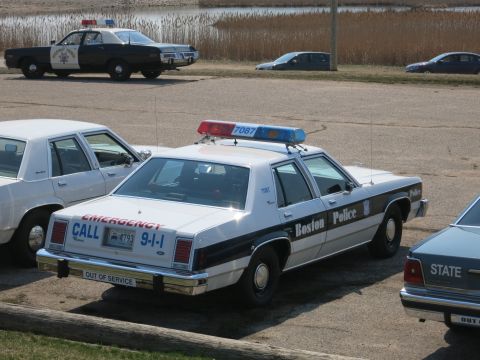 1991 Ford LTD Crown Victoria - Rear quarter view of a Boston Police 'Emergency Call 9-1-1' sedan with a Highway Patrol cruiser parked behind.