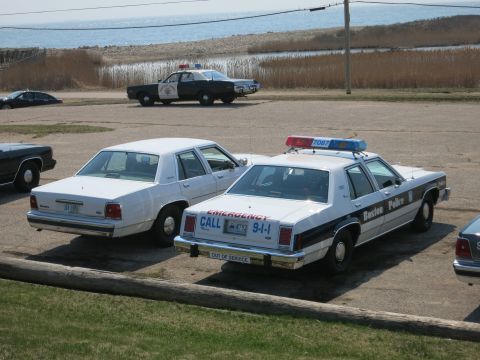 1991 Ford LTD Crown Victoria - Boston Police Ford LTD Crown Victoria with EMERGENCY CALL 9-1-1 livery parked beside a white sedan at a coastal lot.