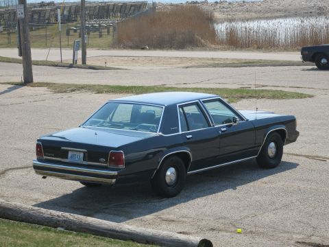 1991 Ford LTD Crown Victoria - dark blue Ford LTD Crown Victoria four-door sedan viewed from the rear three-quarter in a gravel waterfront lot.