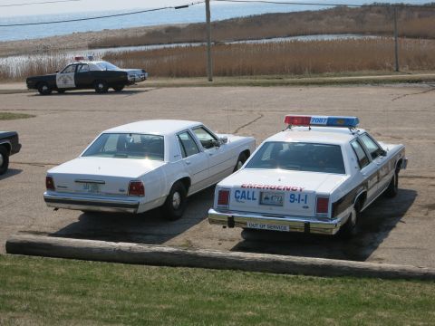 1991 Ford LTD Crown Victoria - Rear view of a Boston Police Ford sedan with EMERGENCY CALL 9-1-1 markings beside a white sedan near the water.