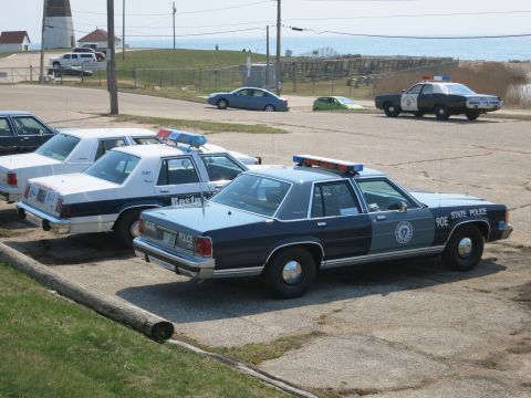 1991 Ford LTD Crown Victoria - State Police Ford sedan marked 90E alongside a Boston Police car in a waterfront parking lot with another cruiser beyond.