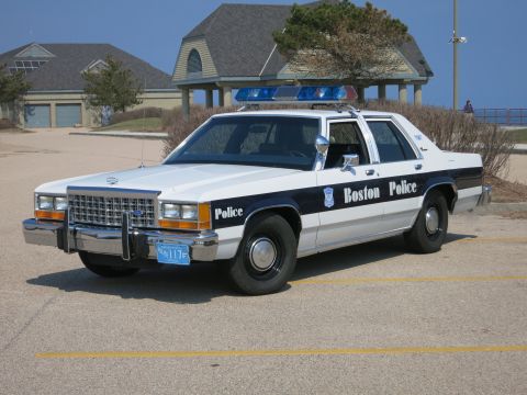 1991 Ford LTD Crown Victoria - white and dark blue Boston Police Ford LTD Crown Victoria sedan parked in a lot with houses and a pavilion behind.