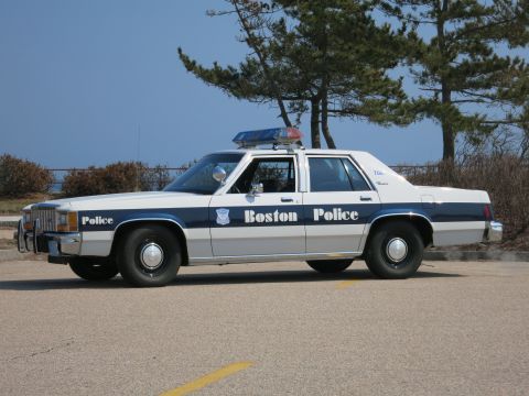 1991 Ford LTD Crown Victoria - Boston Police Ford LTD Crown Victoria sedan in driver-side profile by the shore with trees and clear blue sky.