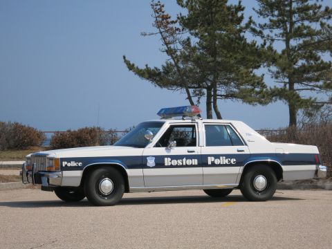 1991 Ford LTD Crown Victoria - Boston Police Ford LTD Crown Victoria sedan in driver-side profile parked along a waterfront lot.