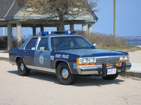 1991 Ford LTD Crown Victoria - blue and silver Ford State Police patrol sedan with push bar and roof light bar parked in front of a colonnaded pavilion.