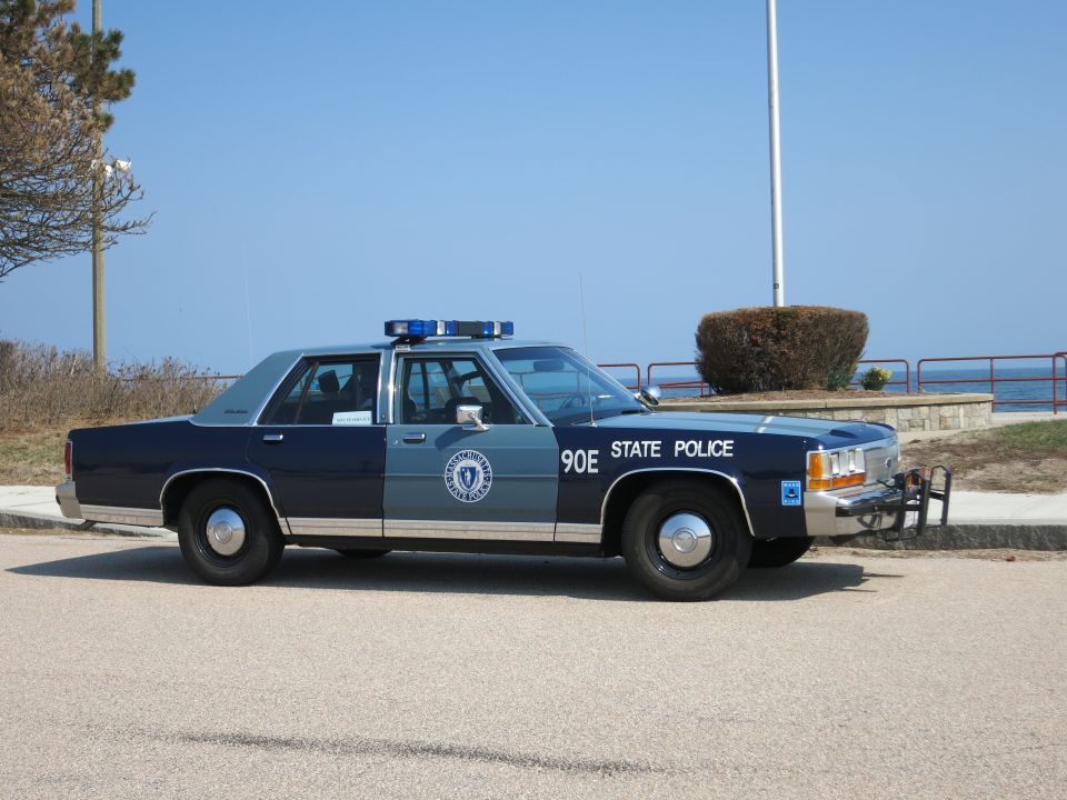 Blue and silver State Police sedan parked beside the ocean