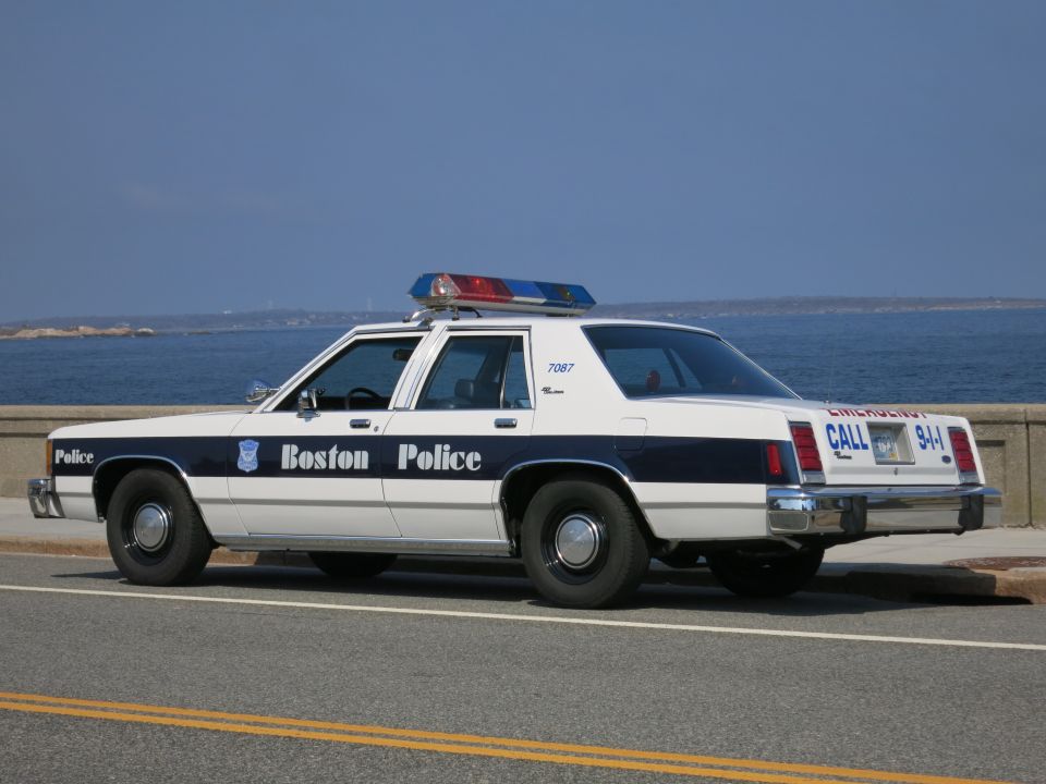 Rear view of a white and blue Boston Police sedan by the ocean