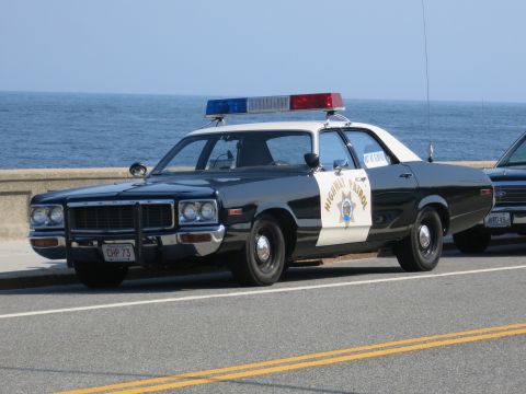1991 Ford LTD Crown Victoria - black-and-white police sedan marked Highway Patrol with the CHP star and plate CHP 73 sits beside a coastal seawall.